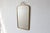 A wall mirror with a rectangular shape that tapers slightly toward the bottom, set within a slender brass frame with...