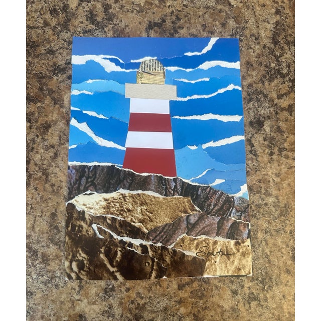 This original mixed-media collage features a bold red-and-white lighthouse standing against a vibrant blue sky, layered...