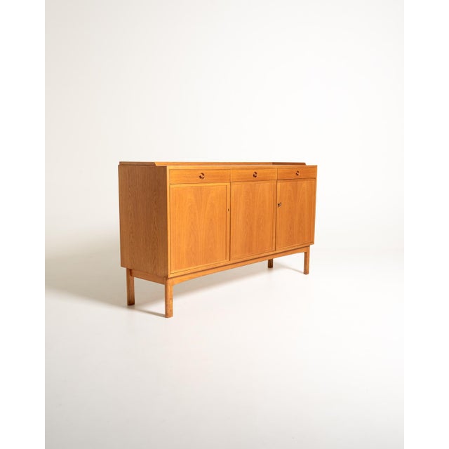 Swedish oak sideboard from the 1960s, produced by Skaraborgs Möbelindustri of Tibro. It features three doors, three upper...
