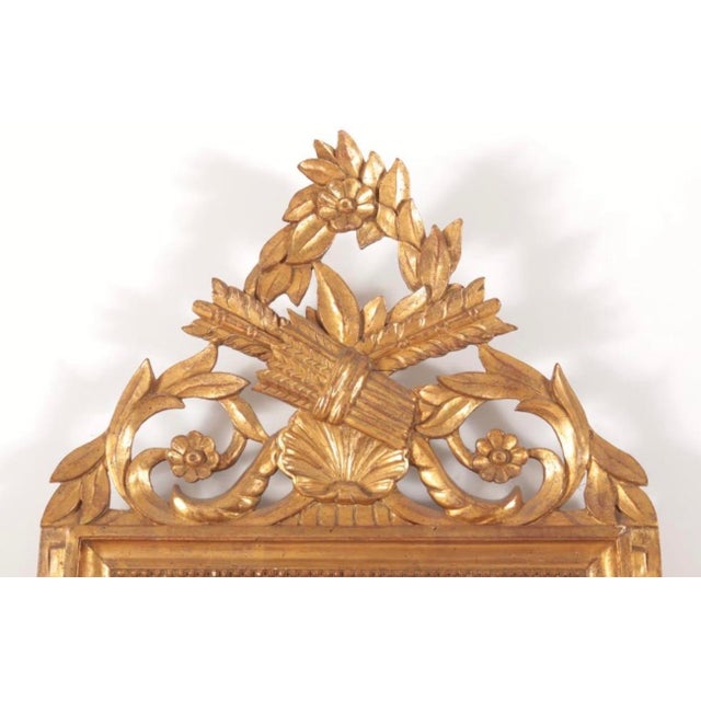 An elegant Italian made Louis XVI-style carved giltwood wall mirror featuring an elaborate openwork floral crest,...