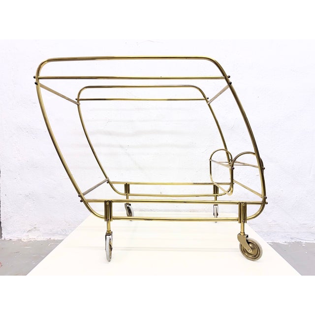 A 1950s bar cart on wheels in a streamlined design with a bottle rack. Brass frame, glass shelves (smoked glass on top,...