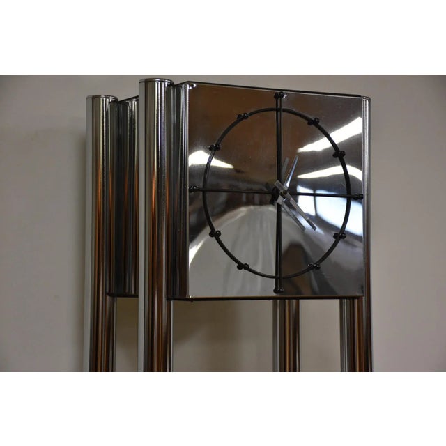 This chrome electric plug in clock has four cylindrical posts with two glass shelves and a black simple modern face. 16”...