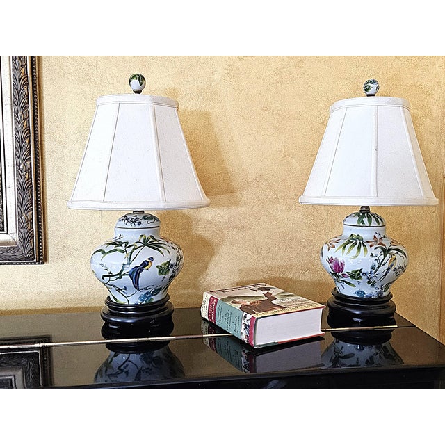Striking pair of vintage Chinoiserie-style porcelain table lamps showcasing finely hand-painted birds and floral motifs on...