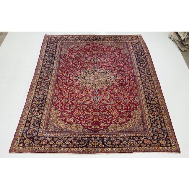 This exquisite Persian Kashan hand-knotted wool rug features a vibrant red field complemented by a navy blue frame. The...
