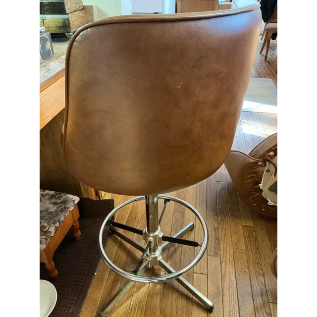 A fantastic pair of vintage 1970s swivel bar stools featuring warm cognac vinyl upholstery and gleaming chrome pedestal...