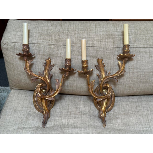 Design Plus Gallery presents a Pair of Gilt Bronze Wall Sconces in the Louis XV Style from the Late 20th Century. They...
