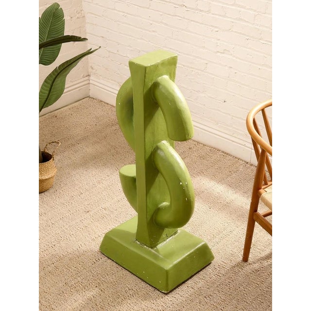 A bold sculptural dollar sign cast in concrete and finished in a punchy lime green. The oversized symbol sits on a...