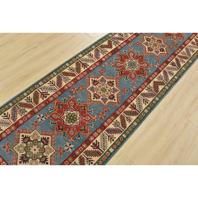 A tribal Caucasian Kazak runner hand-knotted with fine wool on a cotton foundation. This rug features a row of geometric...