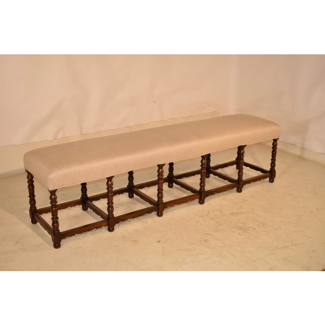 19th century long oak upholstered bench from France. The seat is newly upholstered in linen and is finished with single...