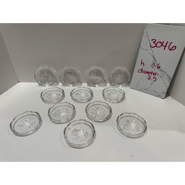 Decorative set of 12 clear glass coasters featuring frosted zodiac symbols representing the astrological signs. Each...