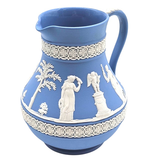 In pale blue stoneware, a garland of white figures encircles the vessel, their gestures frozen in neoclassical grace....