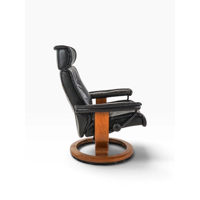 A classic Ekornes Stressless reclining lounge chair with its matching ottoman, in black leather over the early teak-...