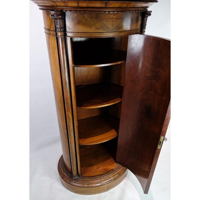 Oval pedestal cabinet decorated with mahogany carvings from around the 1820s. Measurements in cm: H:143 W:71 D:44.