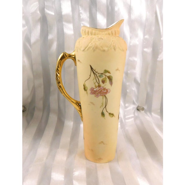 This is a cream matte Royal Rudolstadt pitcher with a gold handle and a purple flower design with a lot of gold trim. The...