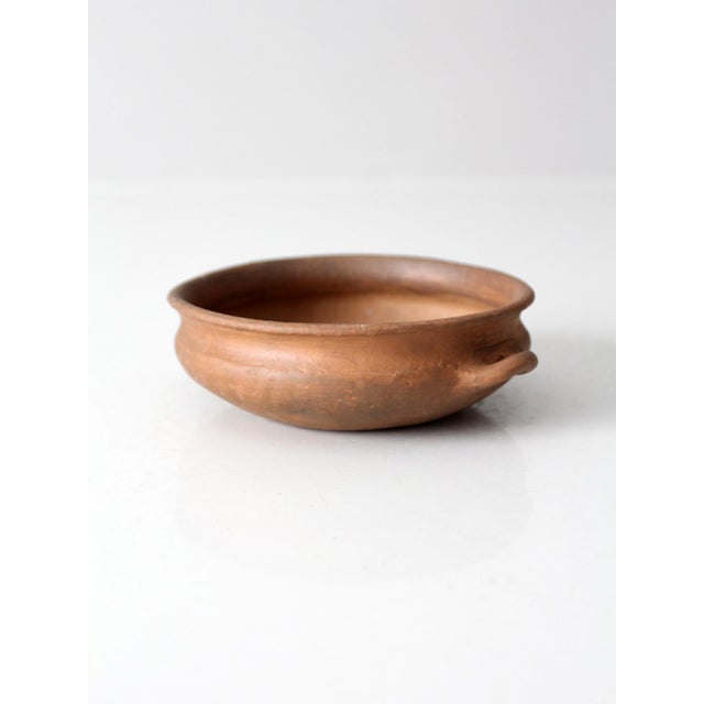 This antique terra cotta bowl has a low, rounded profile with a rolled rim and small loop handles. The unglazed...
