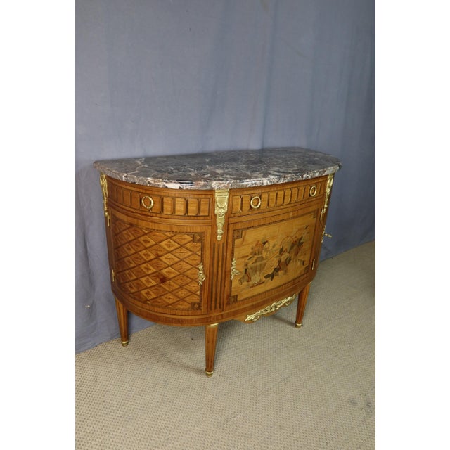 A louis xvi style half-moon commode with doors, dating from the second half of the 20th century. This commode bears the...