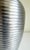 An Art Deco-style ribbed vase crafted from pewter-toned silver metal. It features a sleek, tapered ovoid profile with a...