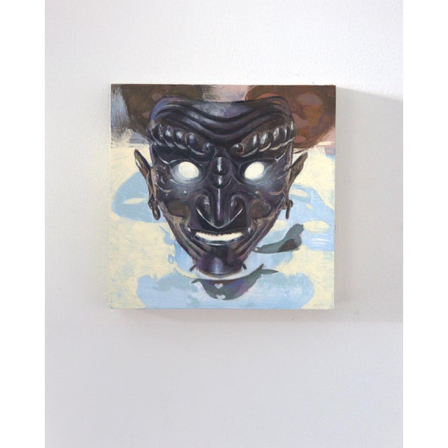 The artwork depicts a striking mask with exaggerated features and luminous eyes, set against a soft, abstract background....