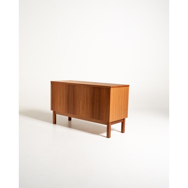 Swedish teak storage cabinet with a side-sliding shutter, two internal compartments, and adjustable metal shelves....