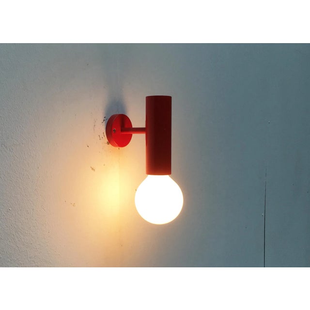2 plain Mid Century wall sconces in a very simple design language. A red cylinder, at the end of which sits the socket for...