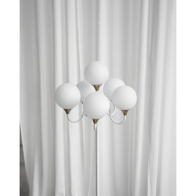A lamp with six opal glass balls on curved arms with a white lacquered structure and brass details that underline its...