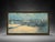 A large framed winter countryside landscape wall art piece featuring a peaceful rural scene with a farmhouse, barn, trees,...