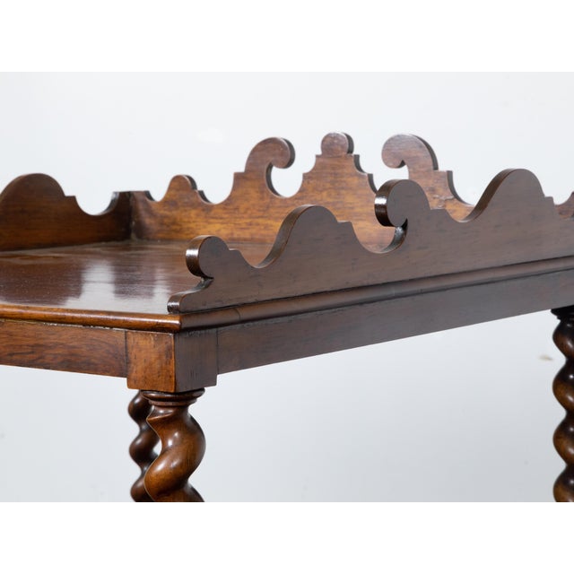 An English walnut barley twist four-tiered shelf with lower drawer, casters and carved three-quarter gallery at the top....