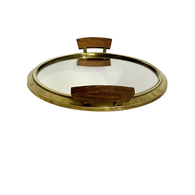 Stylish mid-century modern oval serving tray featuring a warm brass-tone metal frame, a reflective mirrored glass base,...