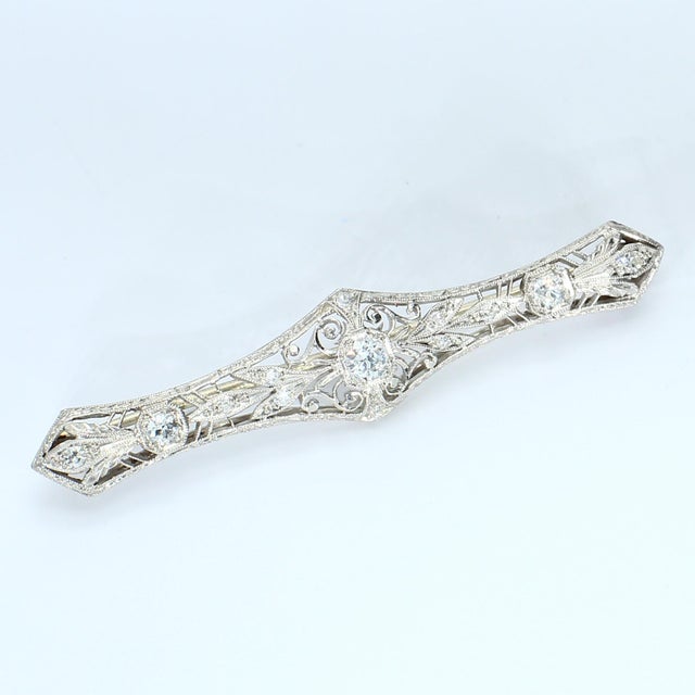 This elongated brooch features intricate filigree work with three prominent diamonds set along its length. The central...