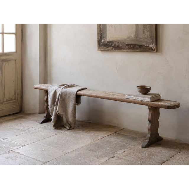 French pine bench, circa 1900, with a long narrow plank seat (219 cm) supported by two sculptural trestle legs and no...