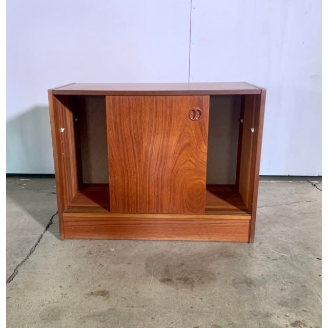 A small vintage sideboard constructed from teak veneer with sliding doors. It features some recessed teak handles and...