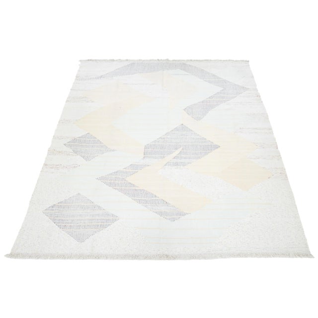 This rug showcases a contemporary Kilim flatweave style crafted from wool. It has a beige field with an abstract motif in...