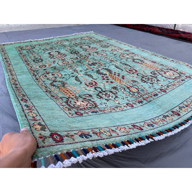 This hand-knotted Oushak rug features an elegant open seafoam-teal field filled with columns of palmettes, rosettes, and...