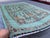 This hand-knotted Oushak rug features an elegant open seafoam-teal field filled with columns of palmettes, rosettes, and...