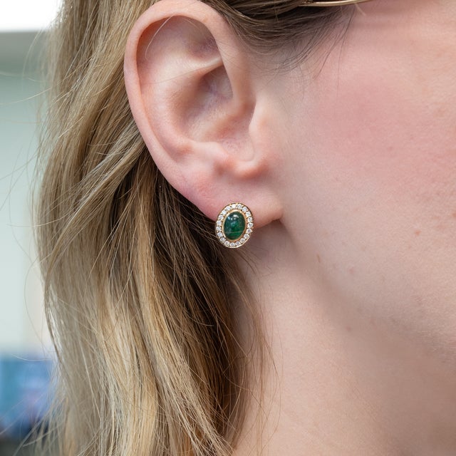 These elegant stud earrings showcase a pair of oval emerald gemstones encircled by a halo of sparkling natural earth mined...