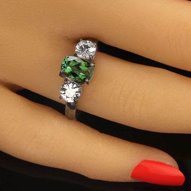 This stunning ring features a vibrant 1.68-carat Brazilian oval green Tourmaline, beautifully complemented by two round...