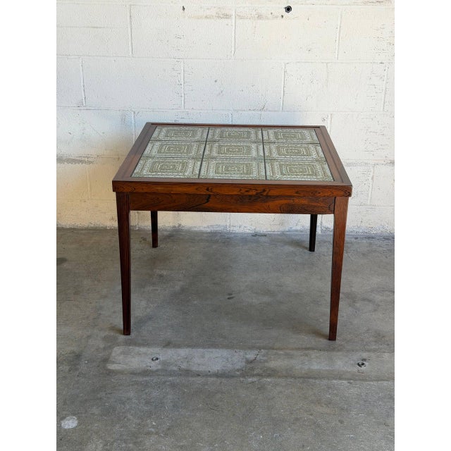 This square side table features a vibrant geometric ceramic tile top inlaid within a rich rosewood frame. Its clean...