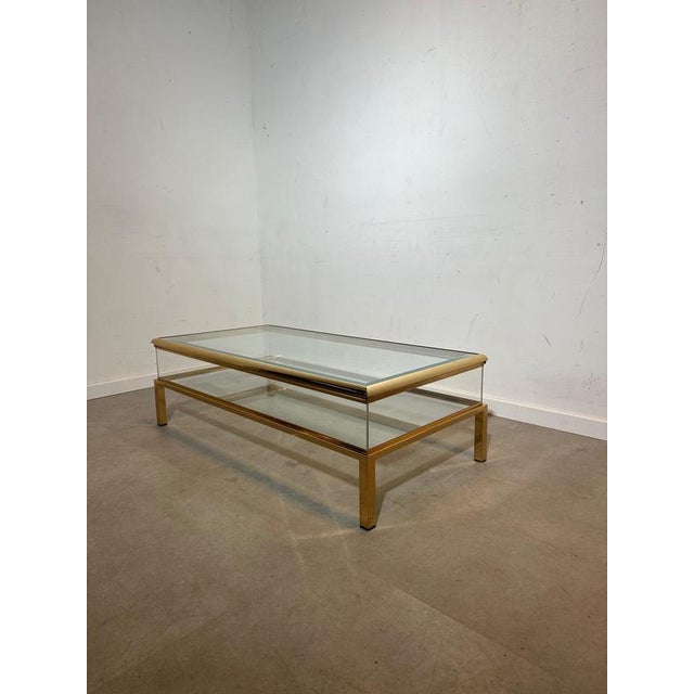Elegant vintage coffee table featuring a refined brass-finished metal frame combined with clear glass surfaces. The design...