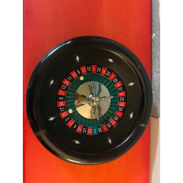 Mid-20th-century roulette wheel with a black lacquered wooden bowl, chromed metal rotor, and alternating red/black...