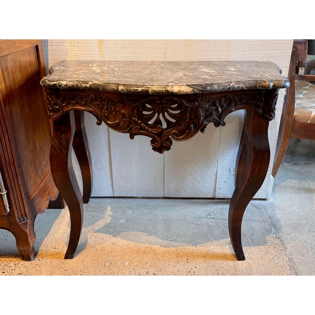 A walnut console of serpentine form, the shaped gray and fawn veined marble top above a deeply carved and pierced apron of...