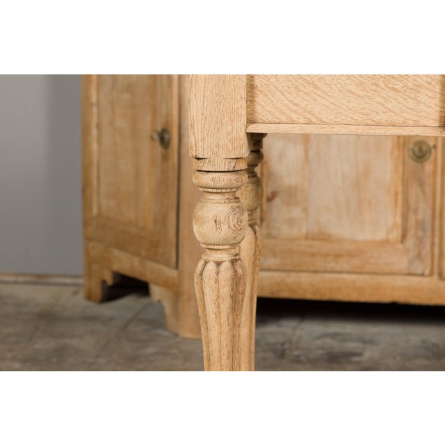 An English bleached oak side table from the 19th century with slightly raised back, single drawer carved with a shield in...