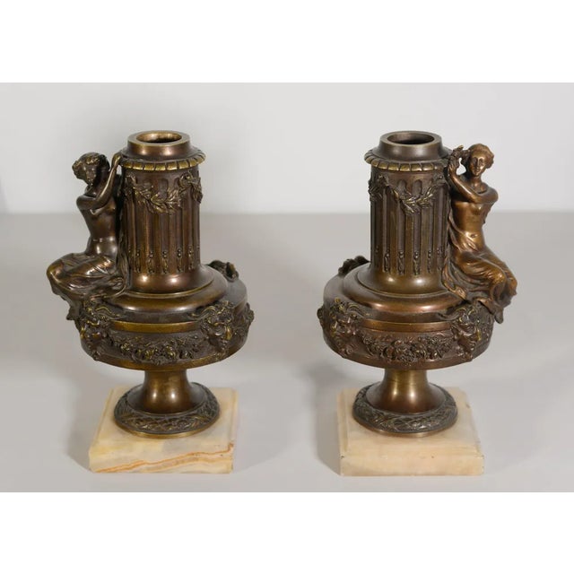 A pair of finely crafted bronze lamp stands featuring fluted columns adorned with laurel garlands and floral wreaths. Each...