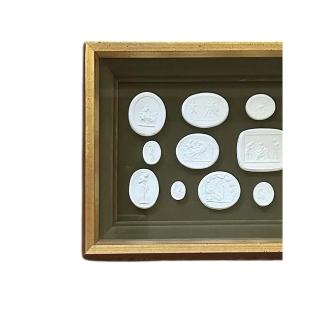 A lovely set of framed grand tour intaglios. Features a collection of 17 white plaster intaglios affixed to a deep moss...