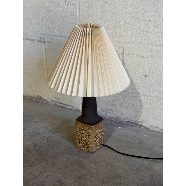 This charming ceramic table lamp features a textured brown base and pleated shade. The warm silhouette brings cozy...