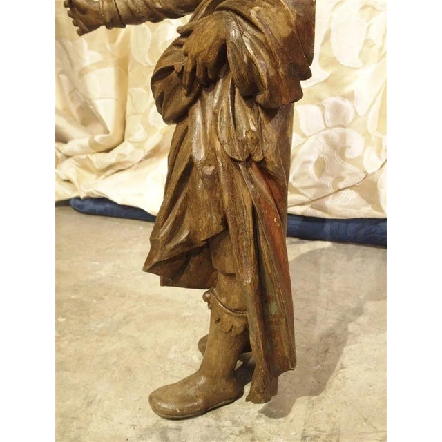 This antique French hand carved wooden statue is of a bearded man wearing a robe tied at the waist with a long scarf...
