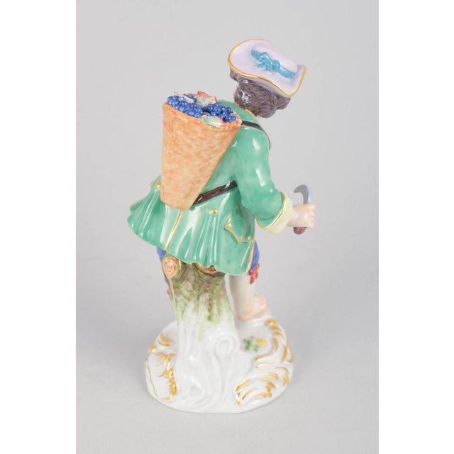 Meissen, grape boy figurine. Porcelain figurine depicting a boy carrying a basket filled with grapes on his back, finely...