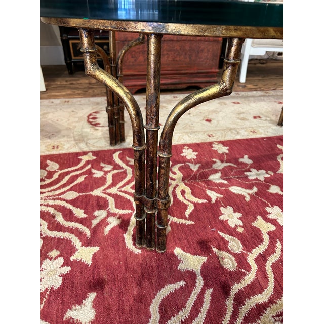 Elegant medium sized oval coffee table having faux bamboo gilded iron base with thick glass top.