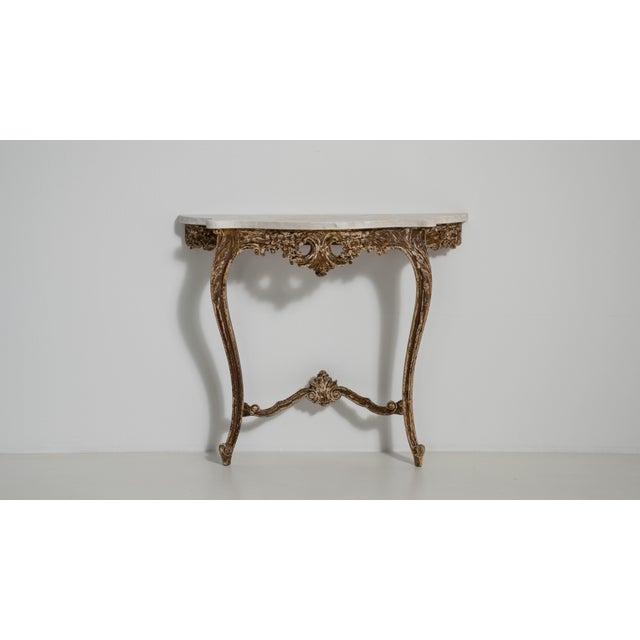 A richly styled console table inspired by Baroque design, featuring curved lines, decorative legs, and a naturally aged...