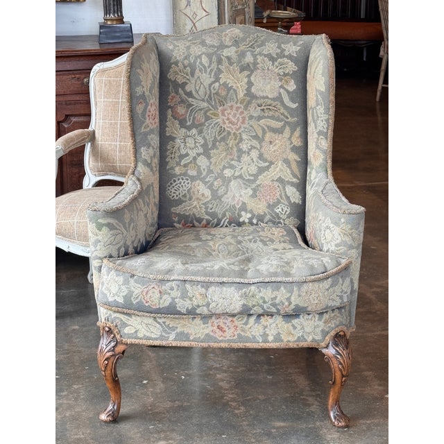 Wingback chair upholstered in floral needlepoint fabric with shaped wings and rolled arms. Loose seat cushion over an...