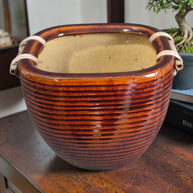 This vintage Asian glazed pottery jardinière planter features a unique square shape with a glossy brown finish and a...